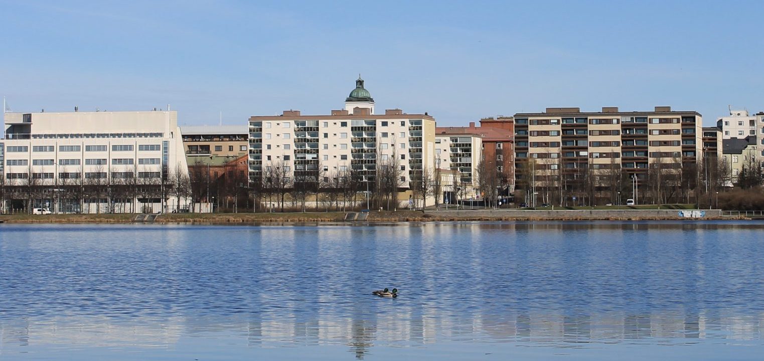 Kaupunki Kantolanniemestä kuvattuna. Edessö Vanajavesi, takana rakennukset. Sininen taivas.